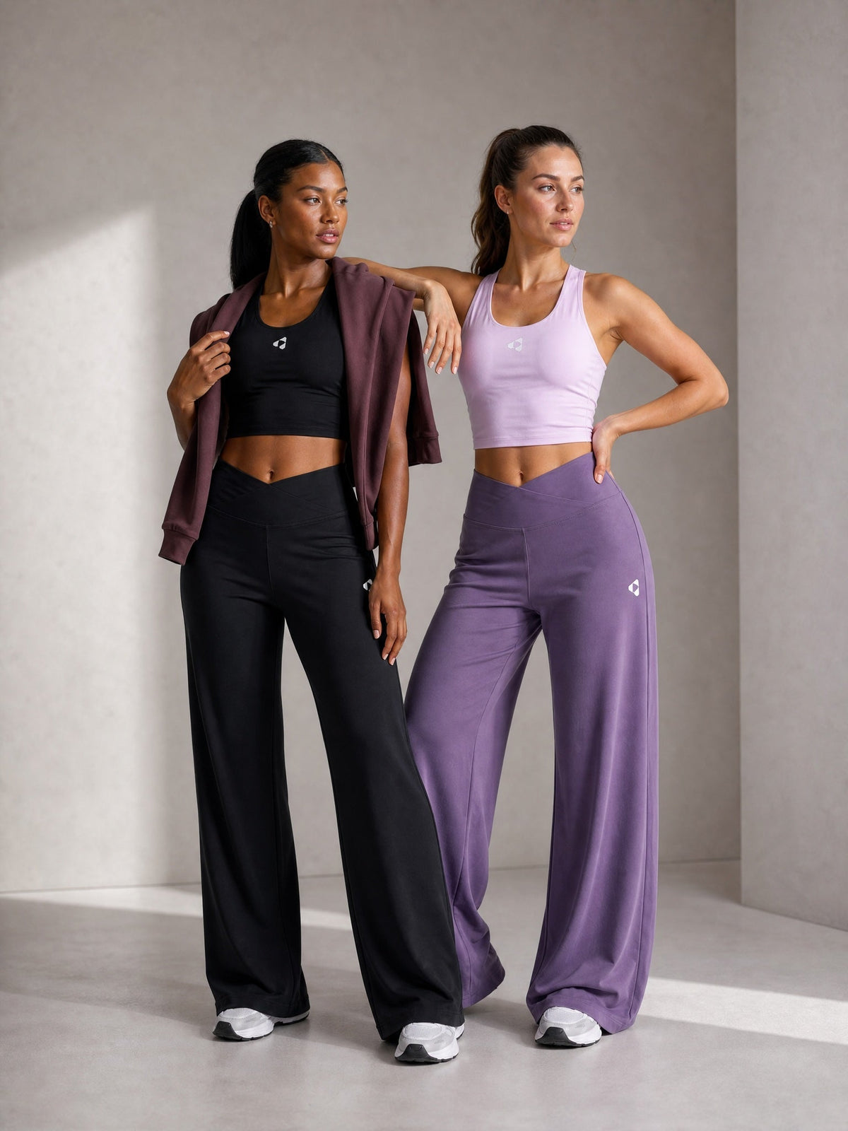 Two women wearing Boost Sportswear crop tops and wide-leg training pants in black and purple.